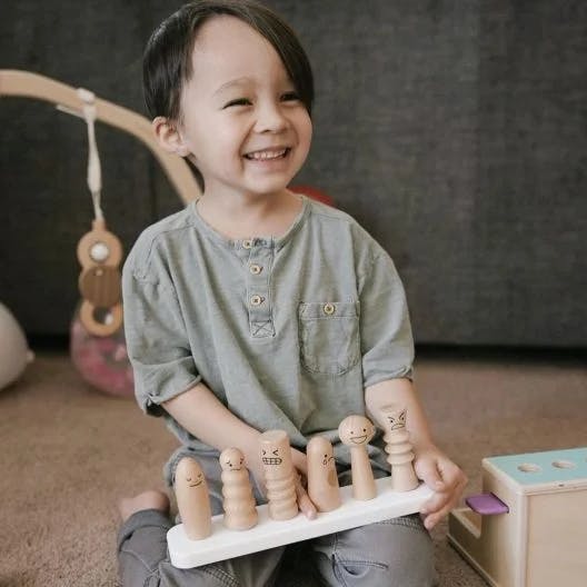 Child holding the Wooden Emotion Dolls from The Observer Play Kit